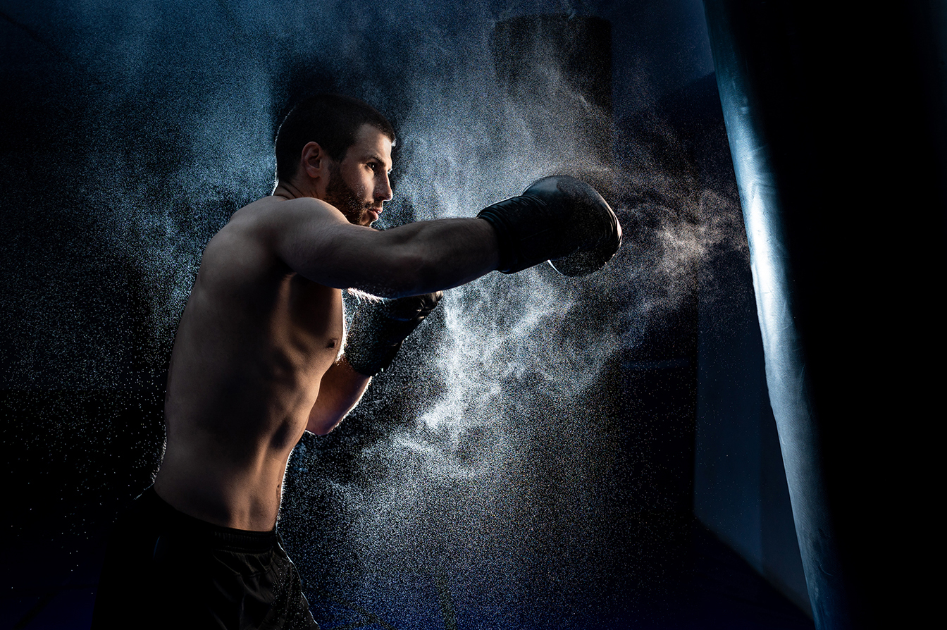 Male boxer boxing in punching bag. shot in smoke. Black background
